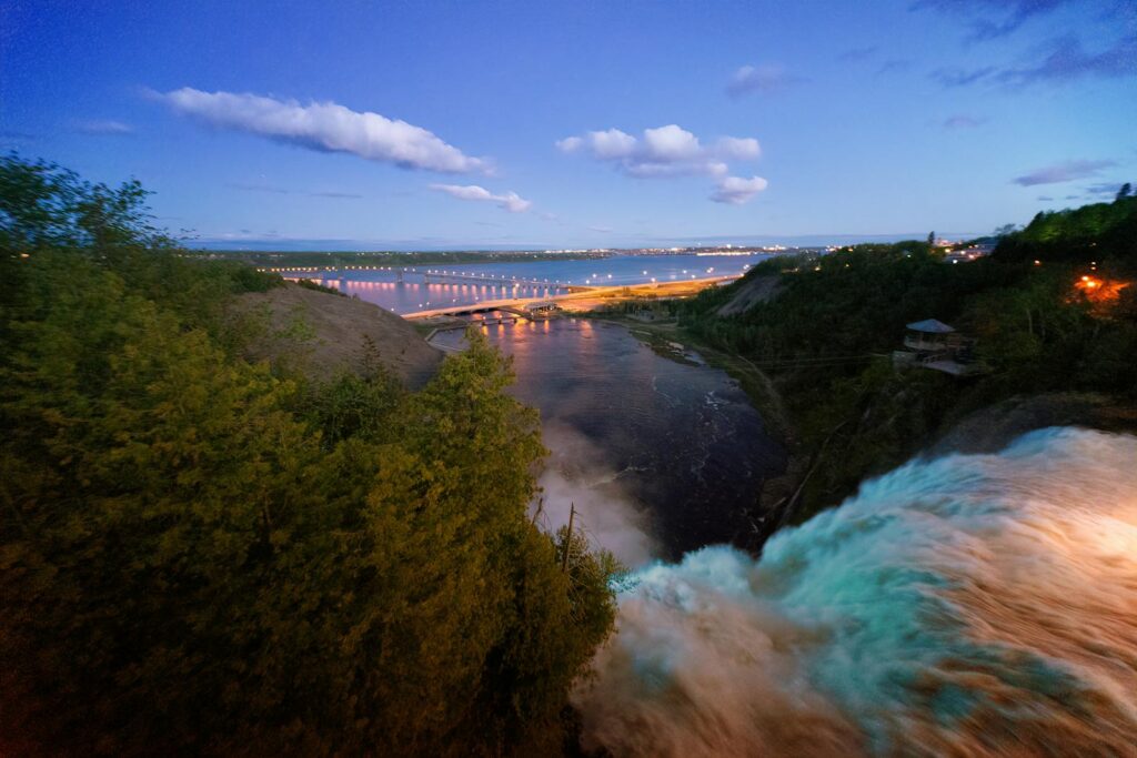 A breathtaking view of a waterfall with a distant cityscape and bridge during twilight.
