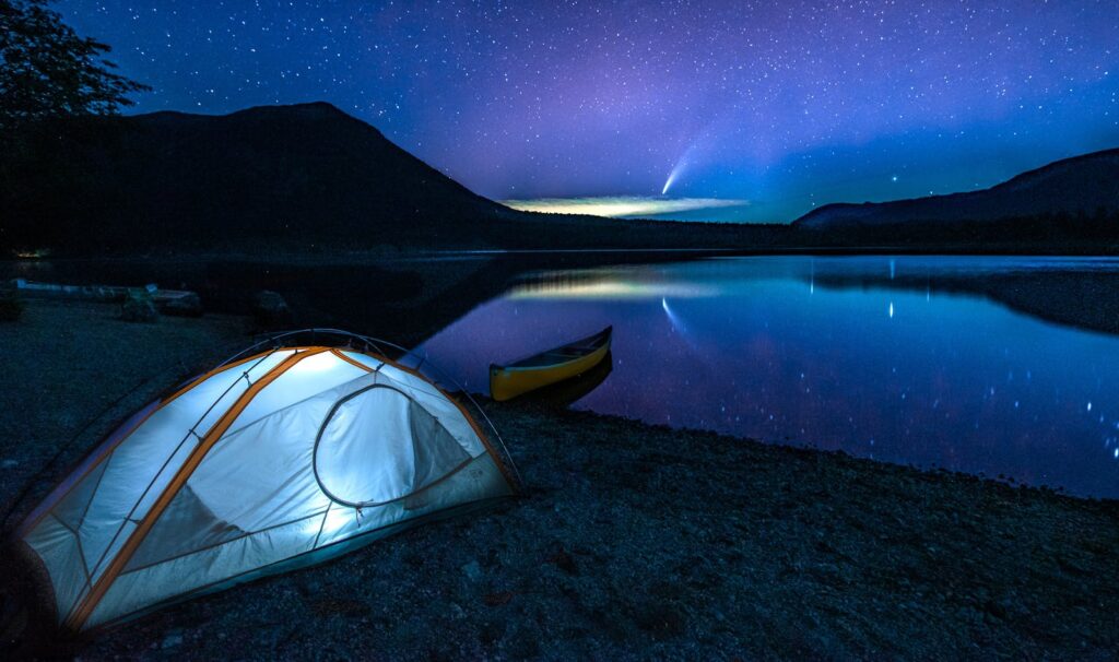 Peaceful camping scene by a lake in Canada under a starry night sky and comet.